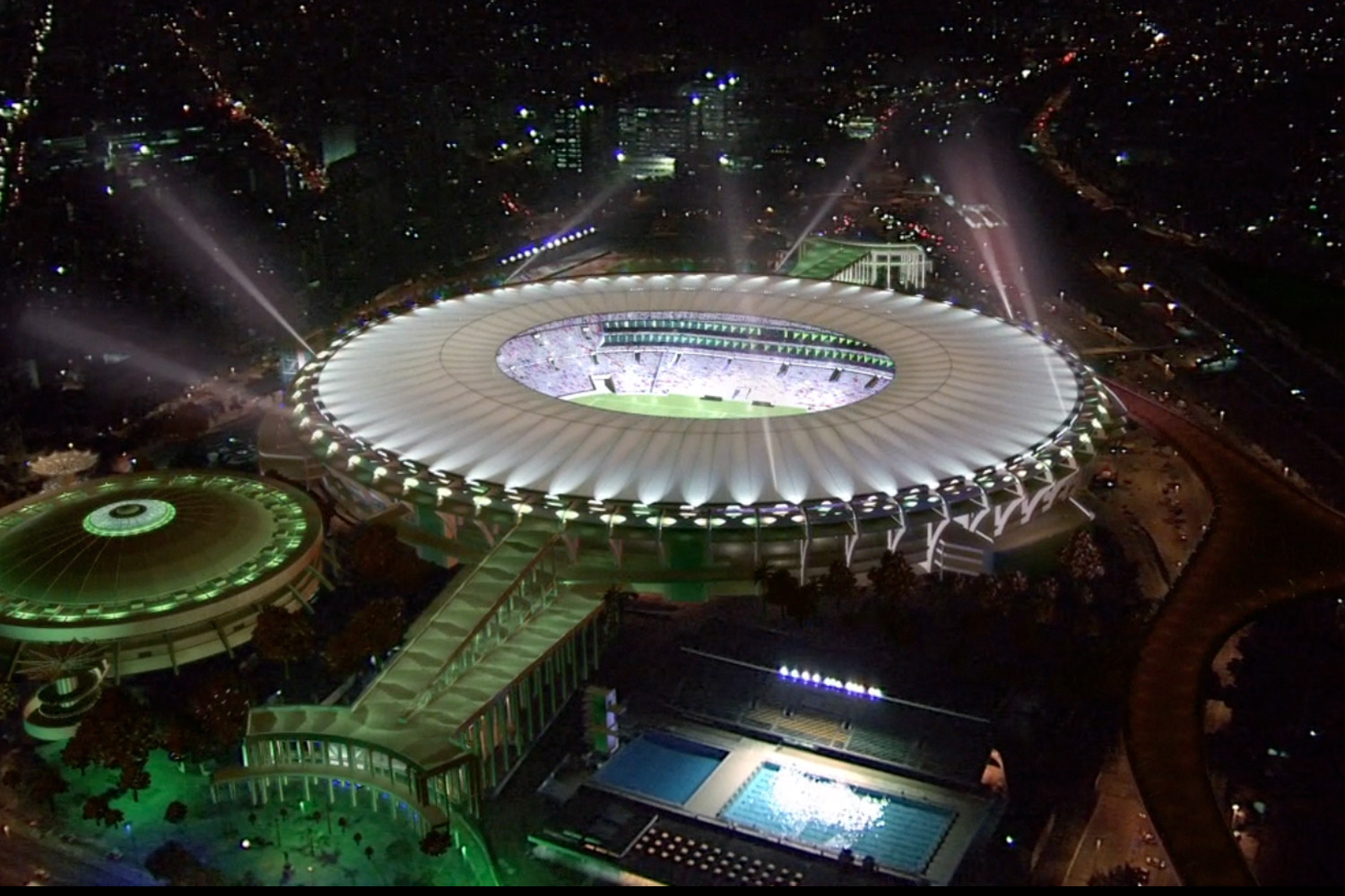 Aerial view of the brightly lit Maracanã Stadium in Rio de Janeiro at night, surrounded by city lights.