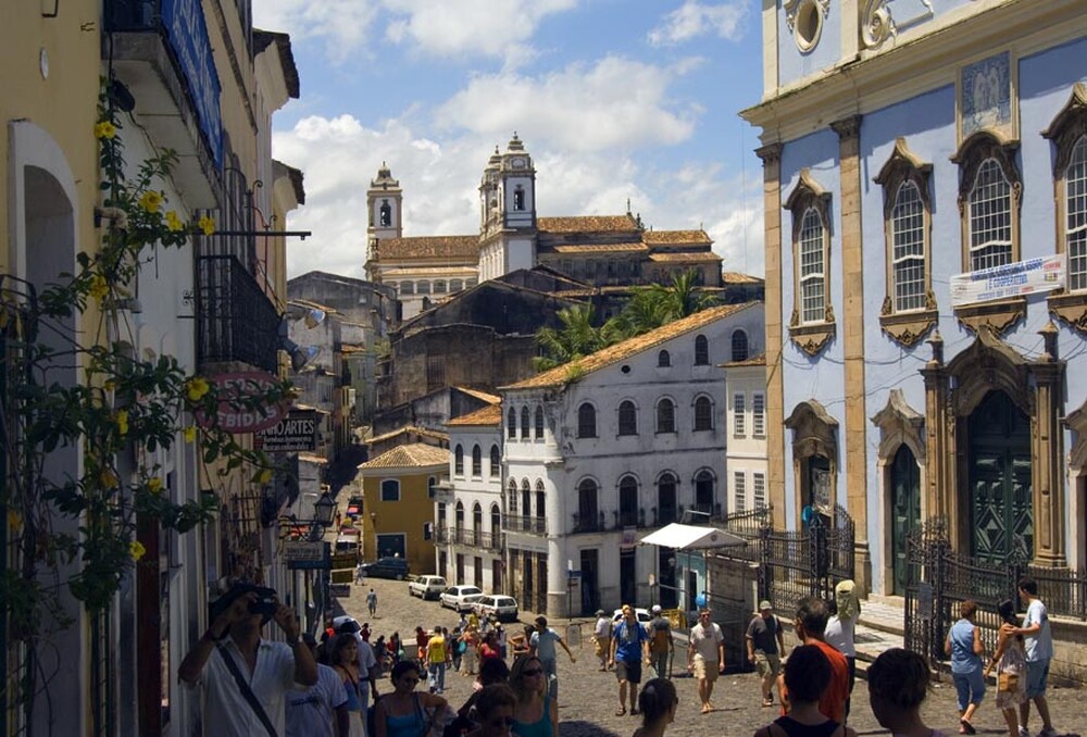 A vibrant street scene in the Historic Center of Salvador, Bahia, Brazil, with colorful colonial buildings and a church in the background.