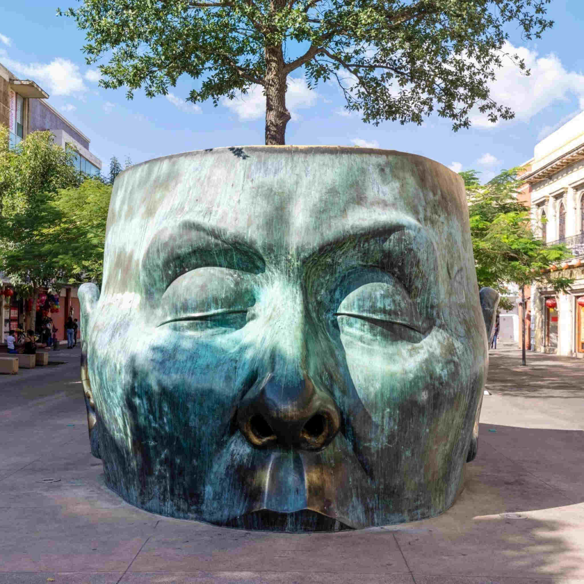 Monumental head sculpture with closed eyes and a tree emerging. Árbol Adentro sculpture in Guadalajara, Mexico.