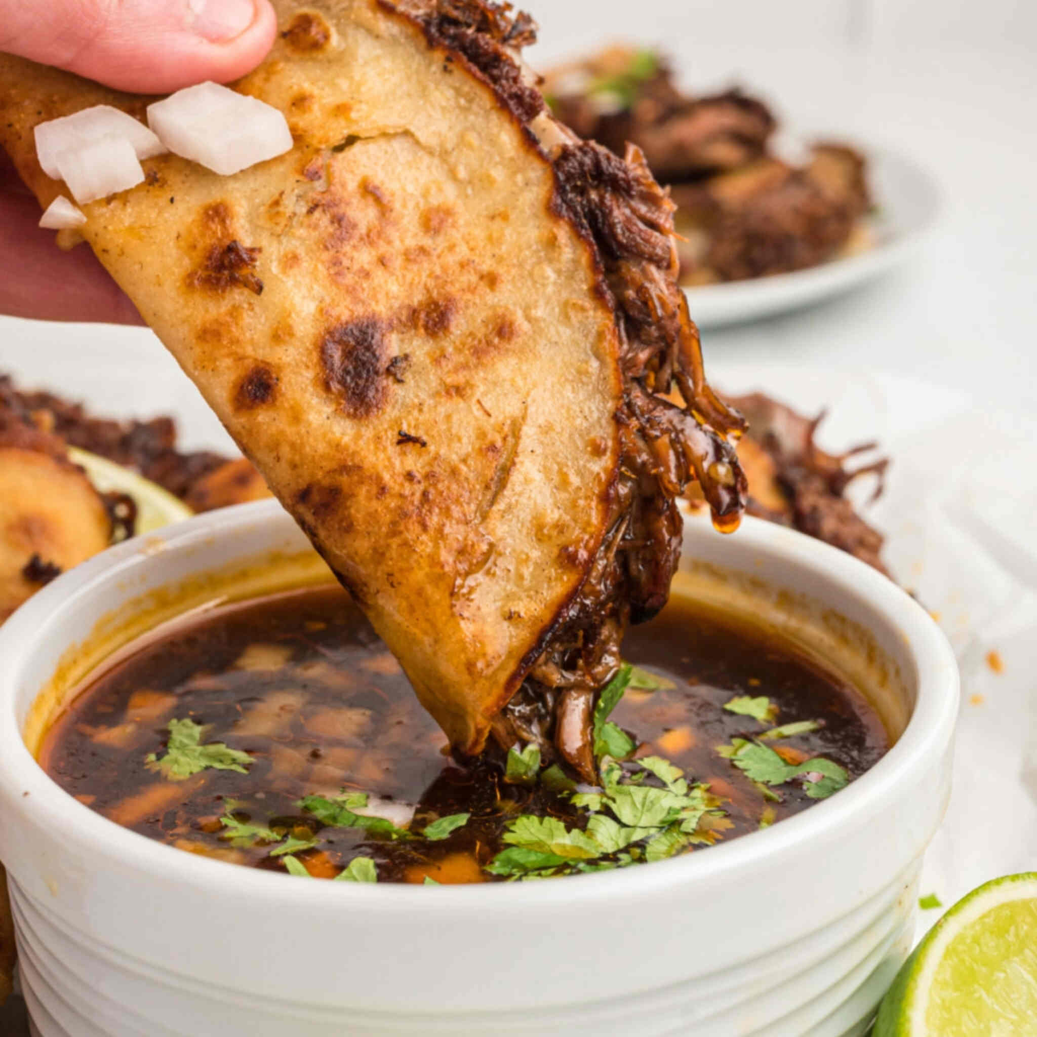 A birria taco being dipped into consommé.