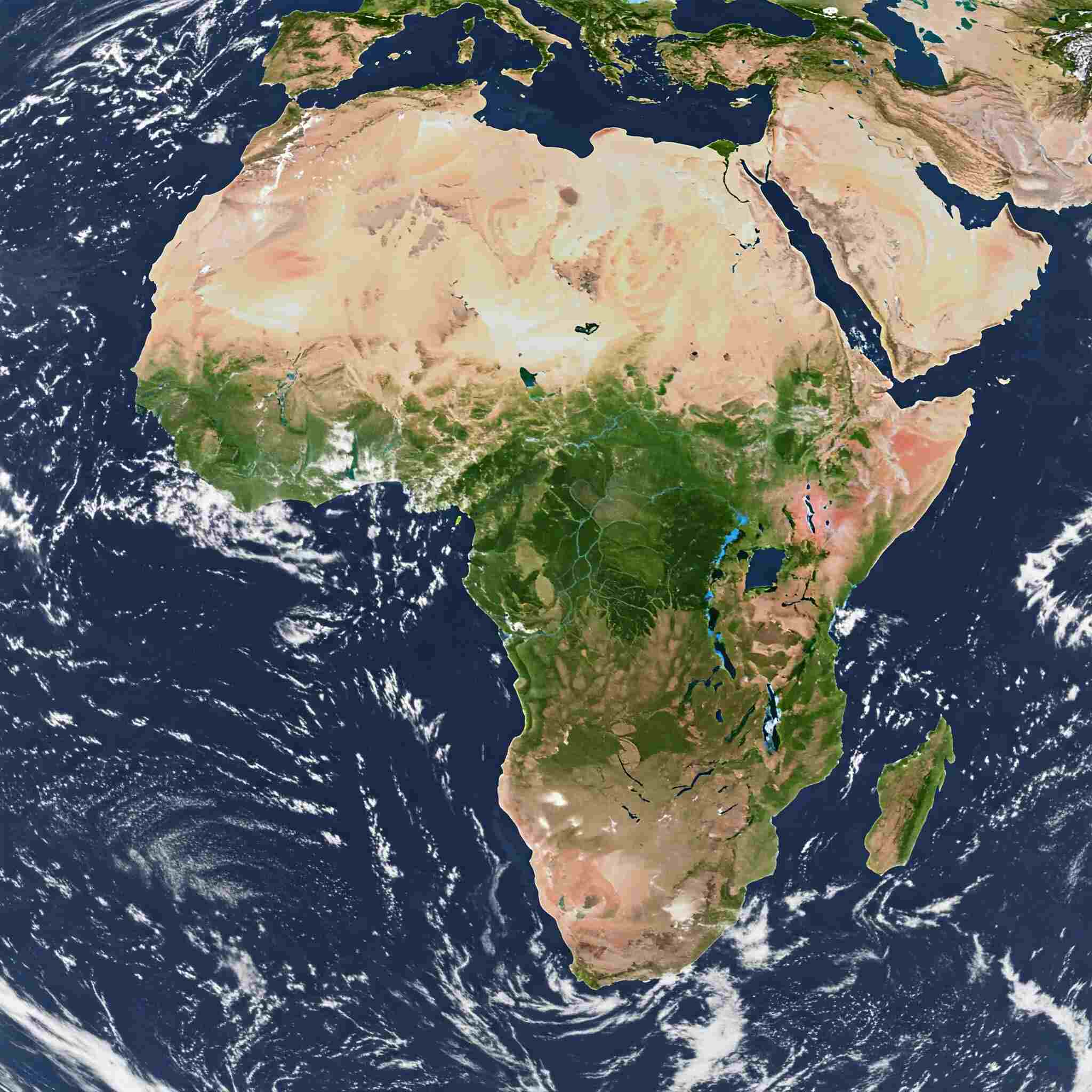 Satellite view of the continent of Africa centered in the frame, surrounded by the blue expanse of the Atlantic and Indian Oceans. Clouds swirl in the atmosphere above the water. The Sahara Desert dominates the northern part of the continent, appearing as a vast expanse of light tan. Moving south, vibrant green hues indicate tropical rainforests and savannas around the equator. The Great Rift Valley is visible as a series of dark lines and elongated lakes in East Africa. The southern tip of the continent shows a mix of green and brown vegetation. The Arabian Peninsula is visible to the northeast, separated by the Red Sea.