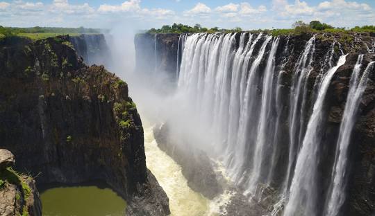 A breathtaking panoramic view of the majestic Victoria Falls, showcasing the immense curtain of water cascading into the gorge, creating a misty spray.